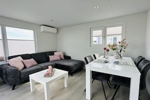 Ein modernes Wohnzimmer mit einem grauen Ecksofa, einem weißen Couchtisch und einem Esstisch mit Stühlen.