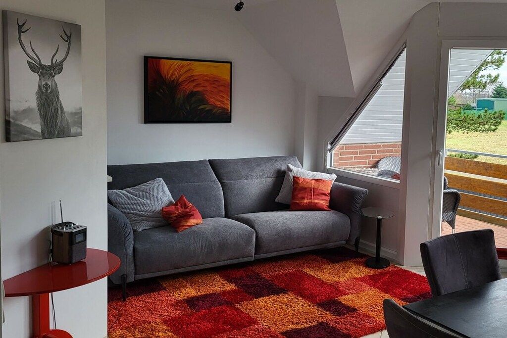 A modern living room with a grey sofa, red and orange patterned rug, and artwork on the walls.