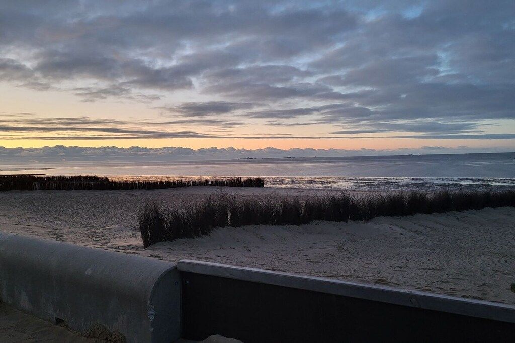 Eine Küstenlandschaft mit Sandstrand, einer Holzstege und einem bewölkten Himmel.