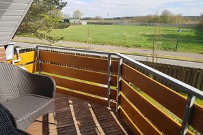 Eine Holzterrasse mit einem Korbstuhl und einem Metallgeländer mit Blick auf ein grünes Feld.