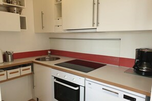 Eine kleine Küche mit weißen Schränken, einer schwarzen Arbeitsplatte, einem eingebauten Backofen und einer Kaffeemaschine.
