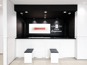 A modern reception desk with a black and white color scheme, a digital display, and two white benches. - Unizo Inn Express Morioka (Morioka)