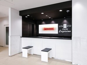 A reception desk with a black and white color scheme, a digital display, and two white stools. - Unizo Inn Express Morioka (Morioka)