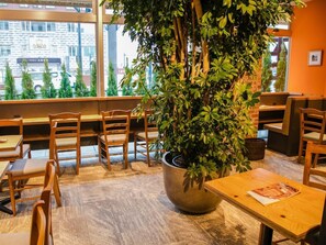 A restaurant interior with wooden chairs and tables, a large potted plant, and a view of the street outside. - Unizo Inn Express Morioka (Morioka)