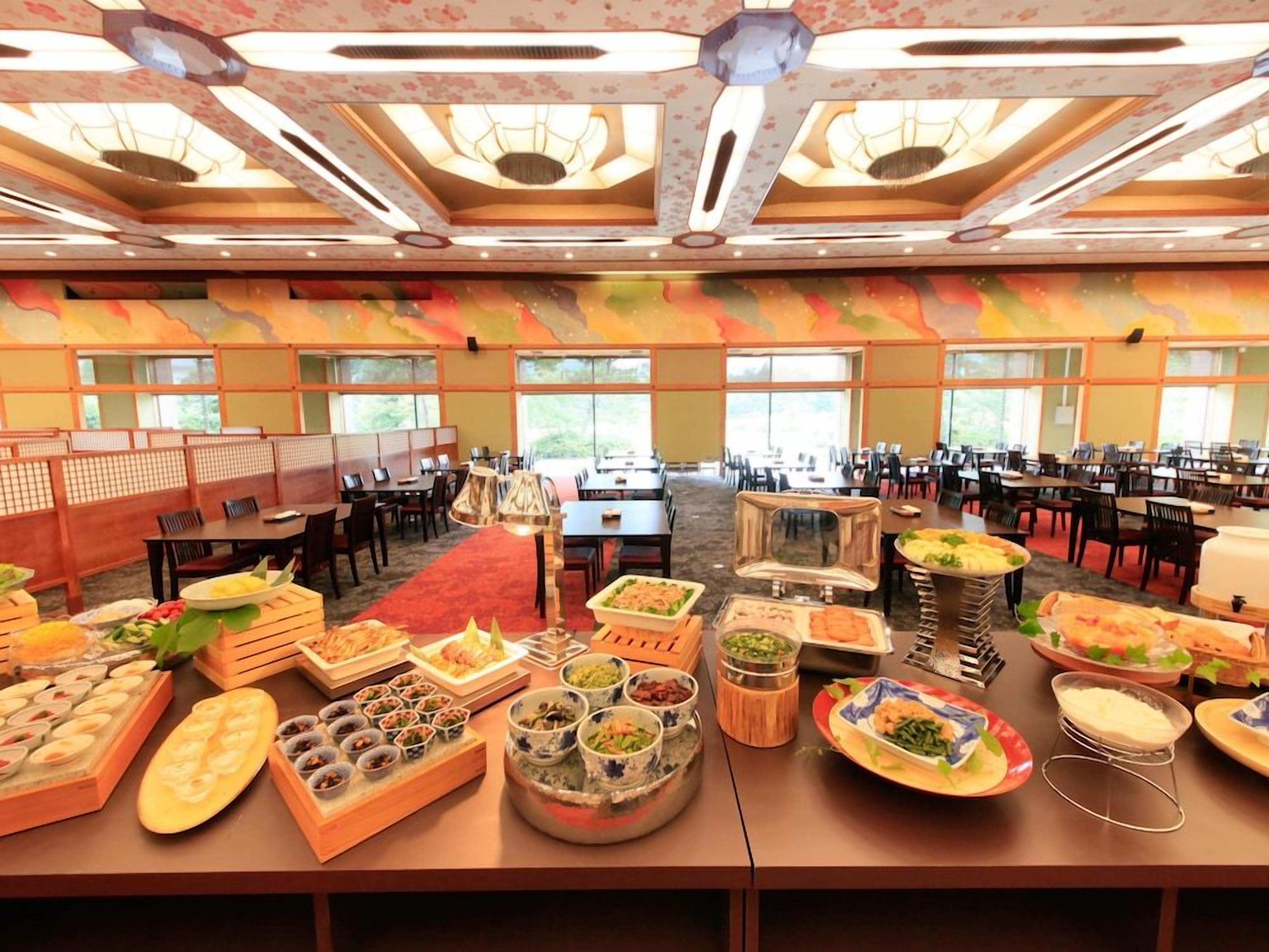 A buffet setup in a hotel dining area with multiple tables and chairs, and a large window providing natural light.