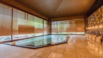 An indoor swimming pool with a wooden ceiling, tiled floor, and a row of potted plants on one side.