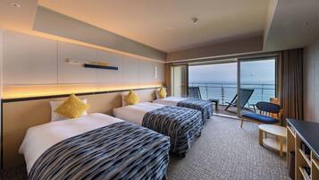 A hotel room with three beds, a desk, and a view of the sea.