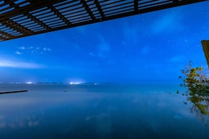 Una noche tranquila con un cielo estrellado sobre una superficie acuática en calma, todo bajo una estructura de madera.