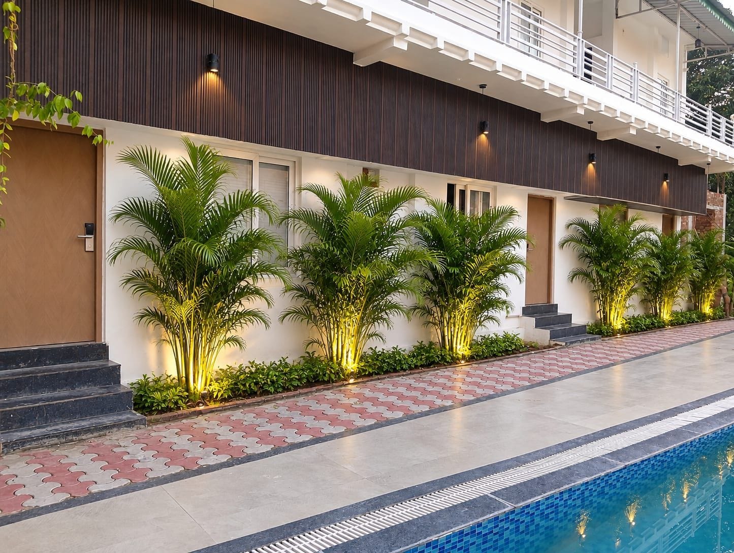 Exterior moderno de un hotel con piscina, plantas en macetas y una entrada bien iluminada.