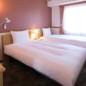 Een hotelkamer met twee bedden, een bedlampje, een nachtkastje en een raam met gordijnen.