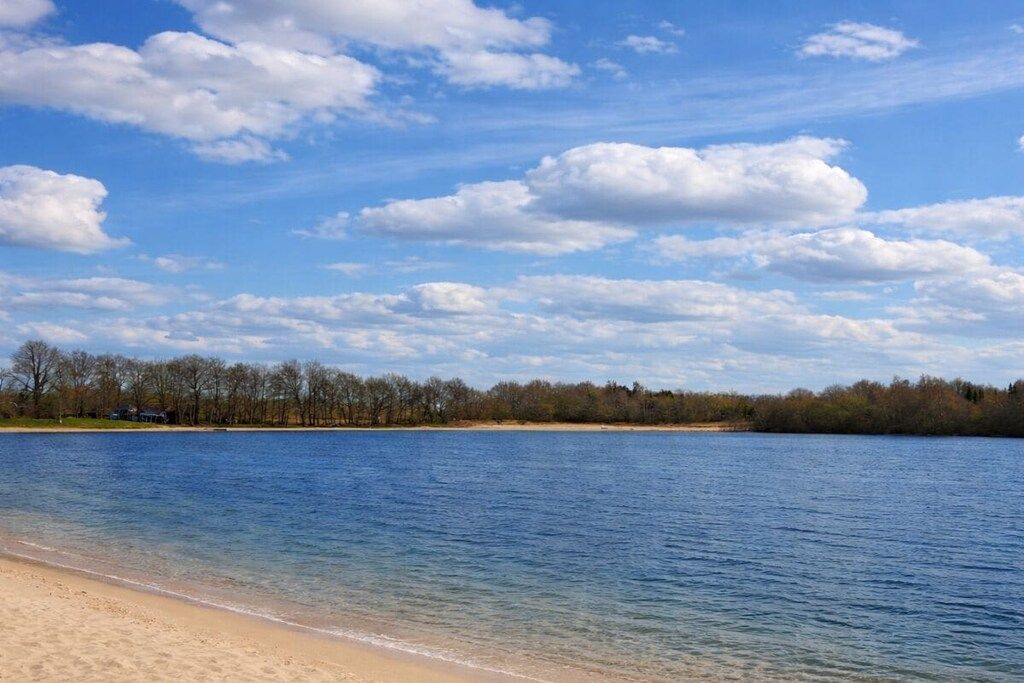 A beach with clear water, a sandy shore, and a line of trees in the background.