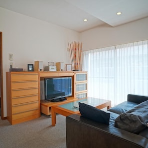 A modern living room with a flat-screen TV, wooden cabinets, a glass coffee table, and a leather sofa. - Tabiyu Abrigo Hotel (Kobe)