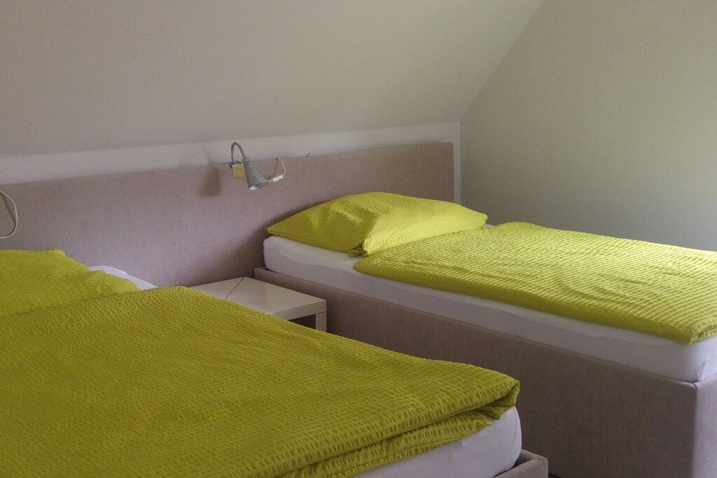 Ein Zimmer mit zwei Betten, jedes mit einer weißen Matratze und einer grünen Decke. Dazwischen steht ein kleiner Nachttisch.