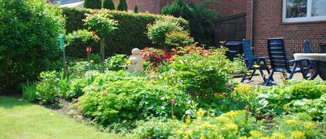A residential garden with a fire hydrant, a hedge, and a brick house with a sloped roof.