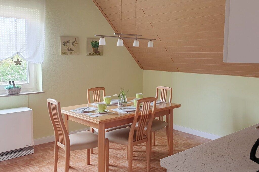 Un coin repas avec une table et des chaises en bois, une fenêtre offrant une vue agréable et un plafond avec des poutres apparentes.