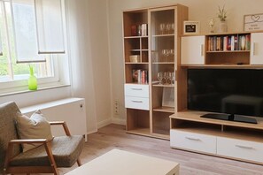 Ein Wohnzimmer mit Fernseher, Bücherregal und einem Fenster mit Pflanze.