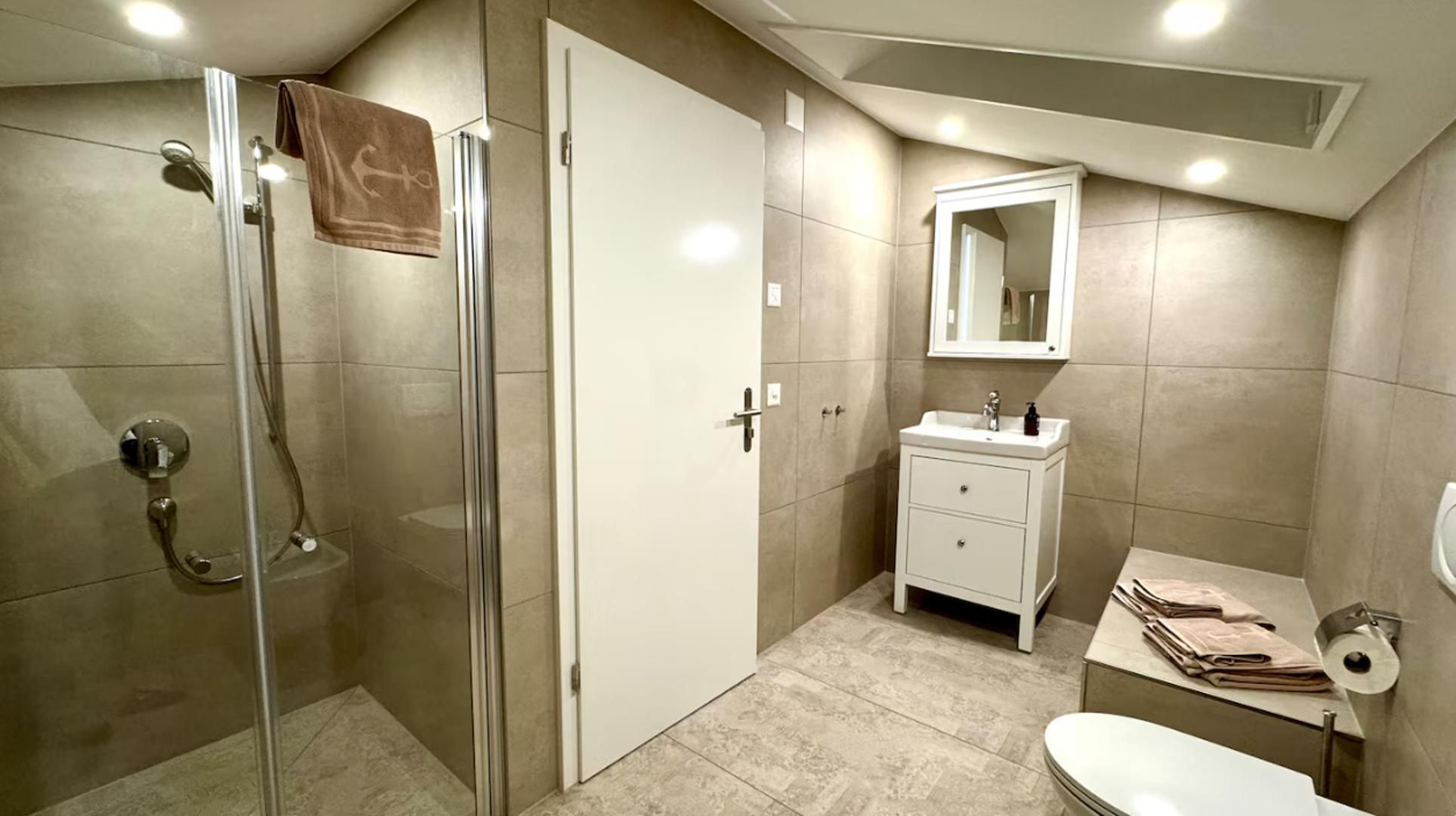 Un baño moderno con cabina de ducha de vidrio, un tocador blanco con espejo y un inodoro.