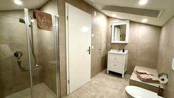 Un baño moderno con cabina de ducha de vidrio, un tocador blanco con espejo y un inodoro.