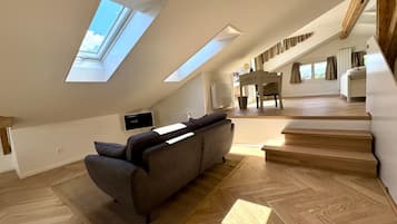 Un loft espacioso con techo inclinado, sofá integrado, zona de comedor y escalera que lleva a un nivel superior.