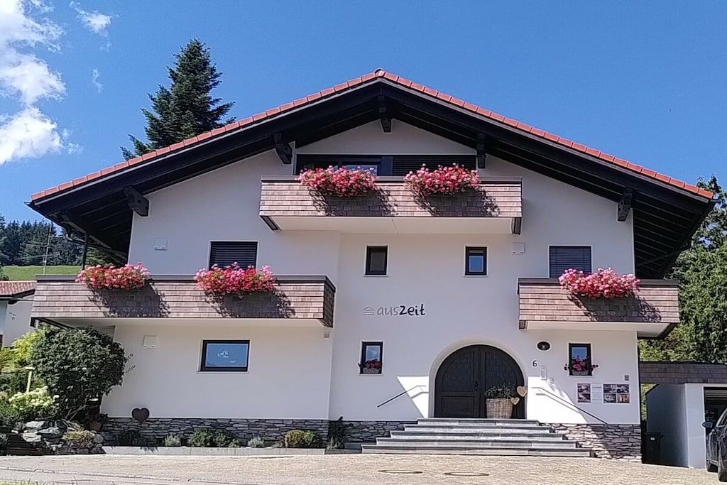 Un edificio de dos plantas con fachada blanca, techo rojo y macetas con flores en los balcones.