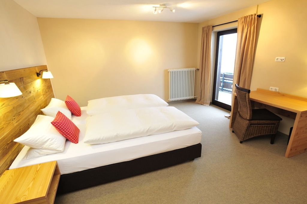 Ein Hotelzimmer mit einem Bett, einem Schreibtisch, einem Stuhl, einem Heizkörper und einem Fenster mit Vorhängen.