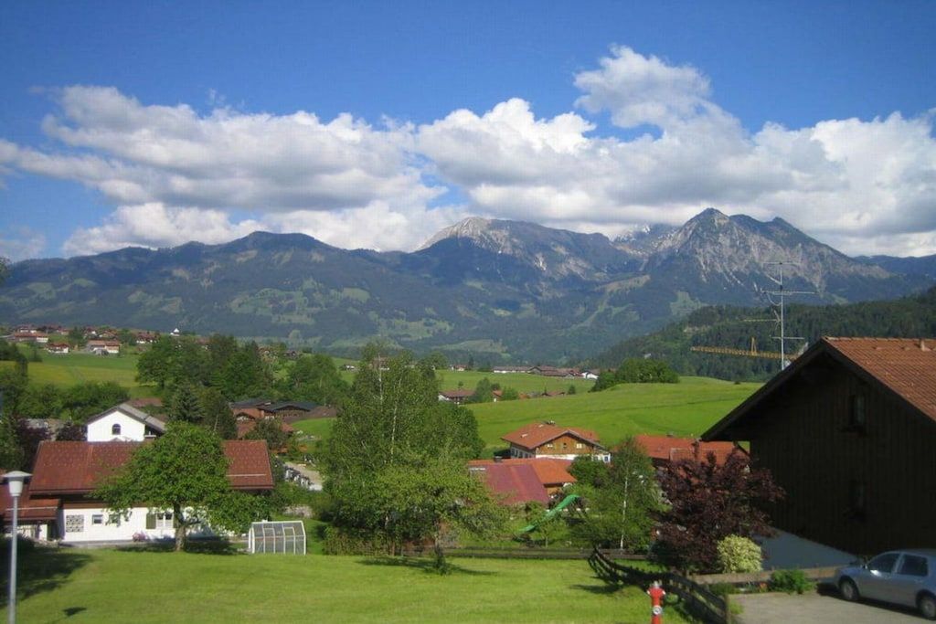 A rural landscape with houses, a barn, and mountains in the background.