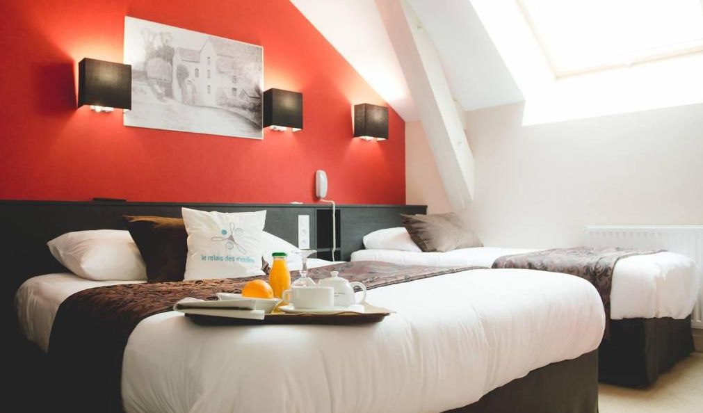 A hotel room with two beds, a red accent wall, and a skylight.