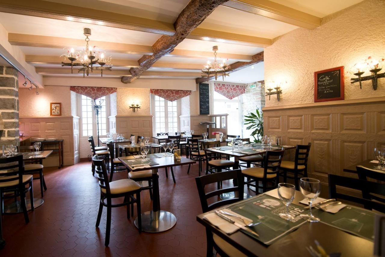 A restaurant interior with multiple dining tables and chairs, wooden beams on the ceiling, and a chalkboard menu on the wall.