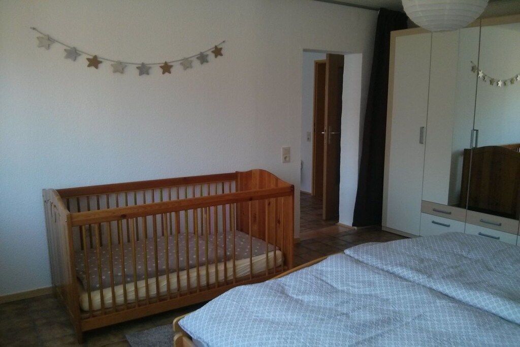 Ein Zimmer mit einem Reisebett, einem Bett, einem Kleiderschrank und einer Tür zu einem weiteren Raum.