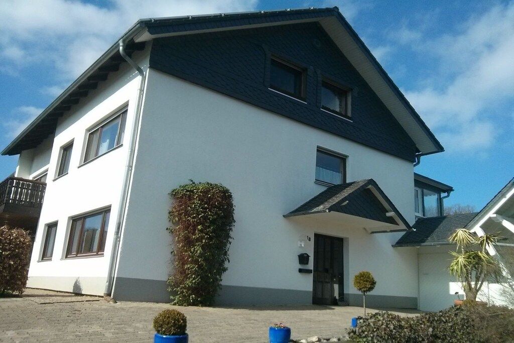 Een herenhuis met een donker dak, witte muren en een klein voortuintje.