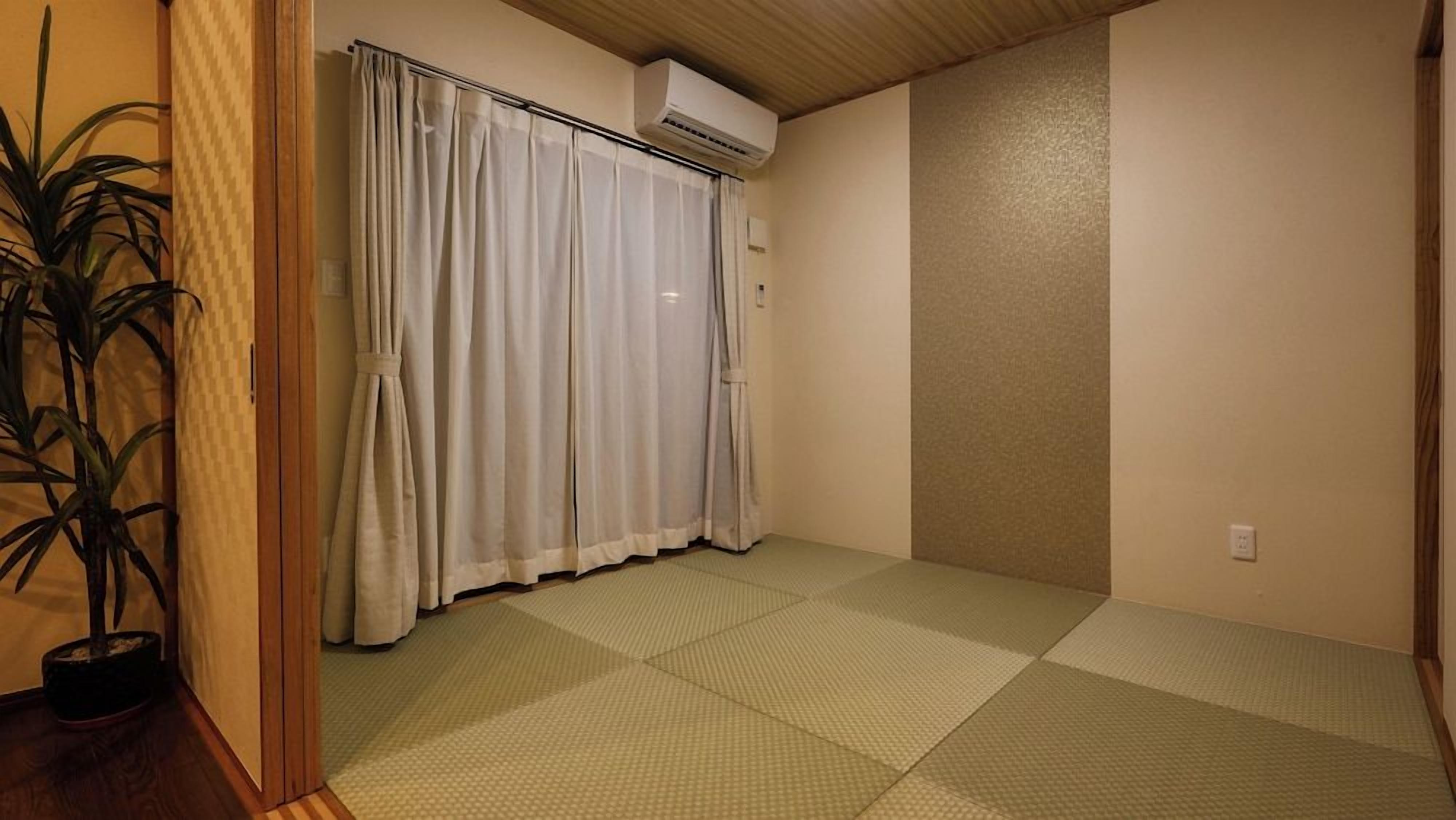 Una stanza con pavimento in tatami, una porta scorrevole con tende, un condizionatore d'aria e una pianta in vaso.
