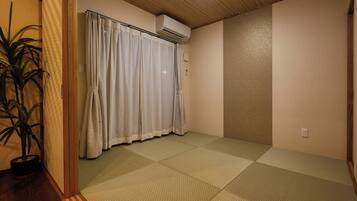 A room with tatami flooring, a sliding door with curtains, an air conditioning unit, and a potted plant.