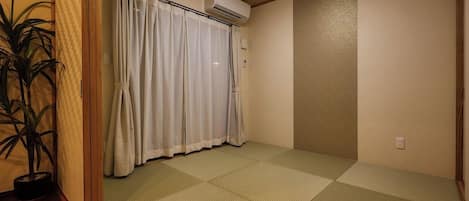 Una habitación con suelo de tatami, una puerta corredera con cortinas, un equipo de aire acondicionado y una planta en maceta.