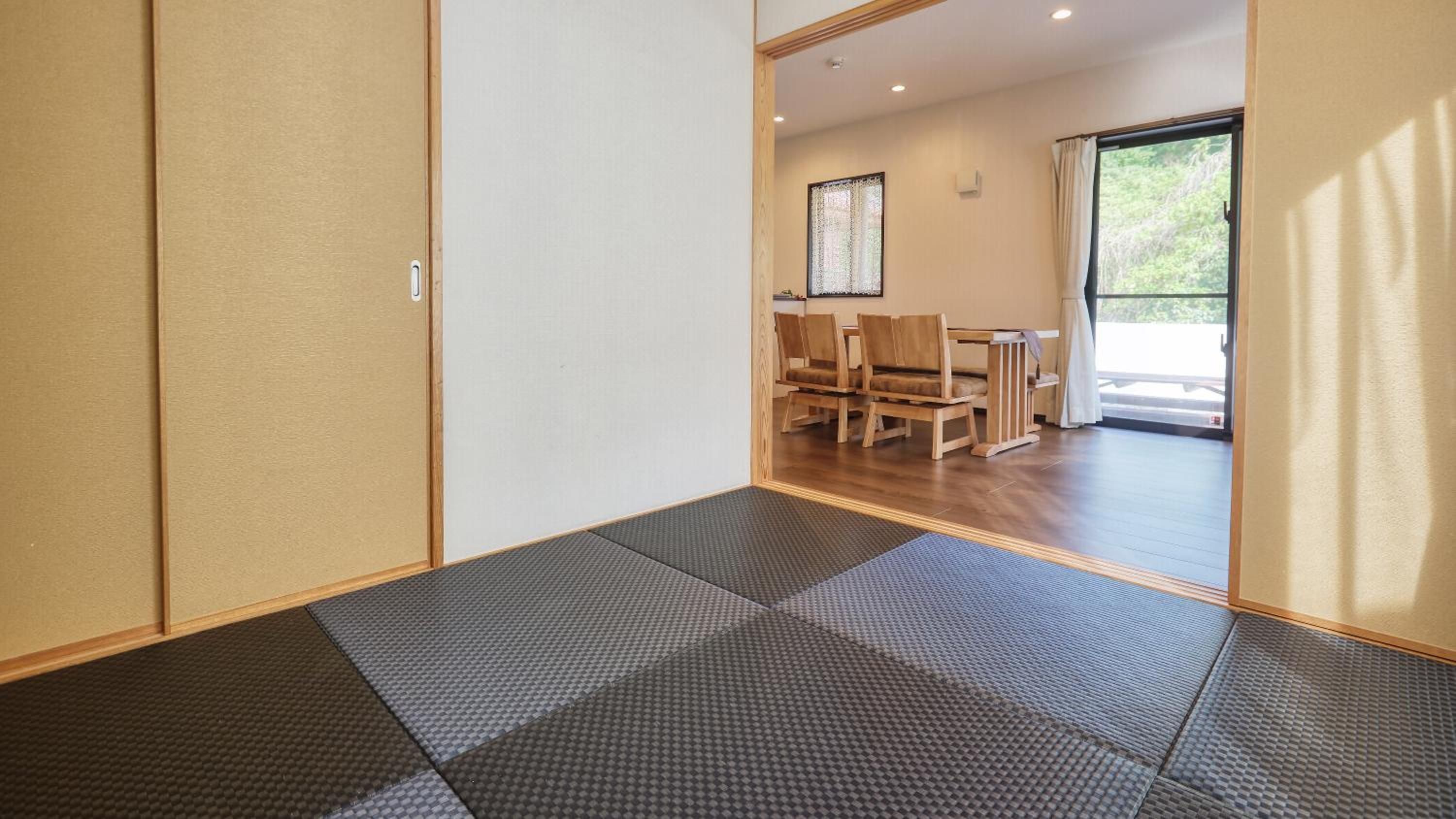 A room with tatami mats, a wooden table with chairs, and a sliding door.