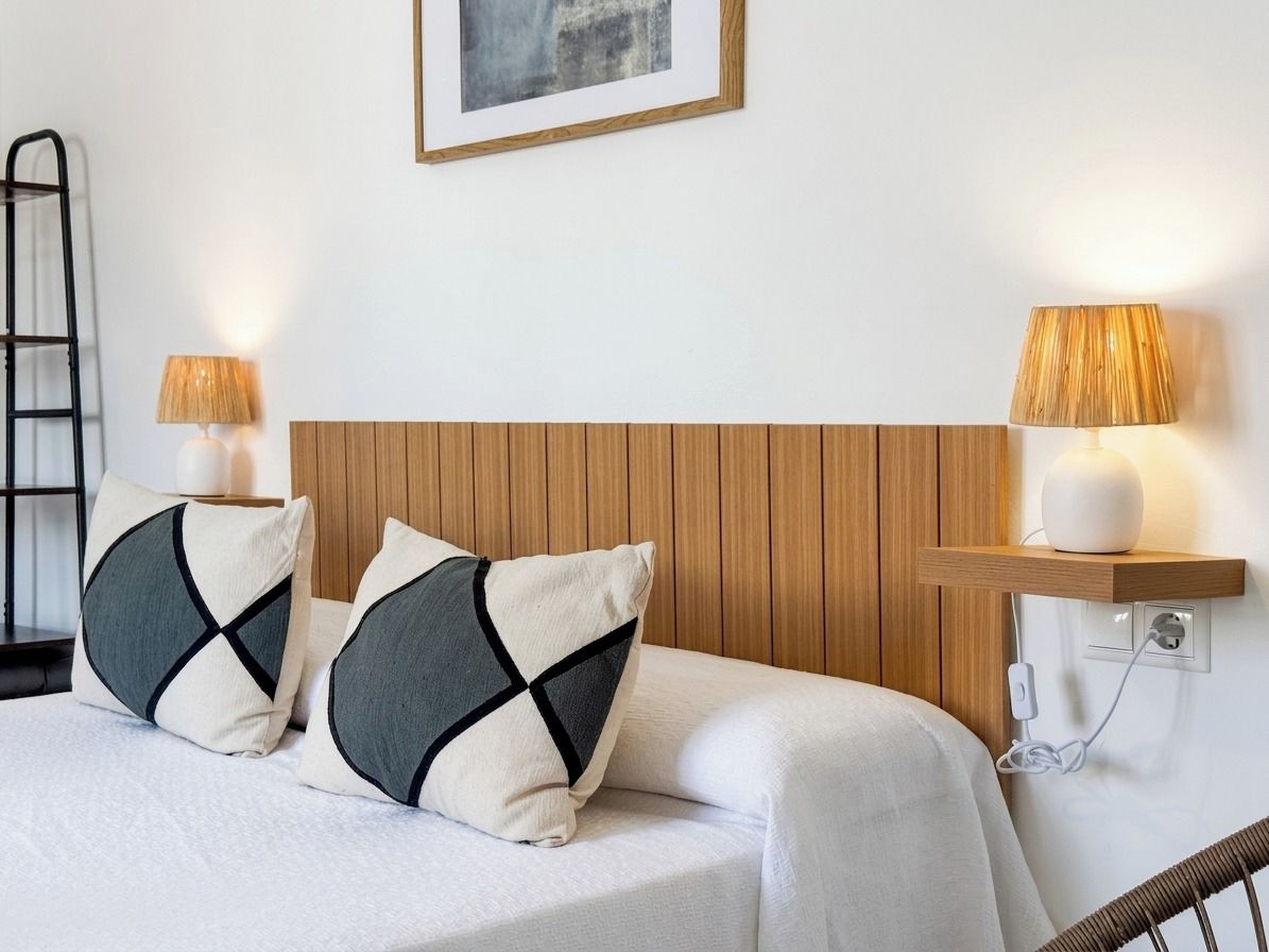 Un lit bien fait, avec deux oreillers, une tête de lit en bois, des lampes de chevet et une prise électrique sur le mur.