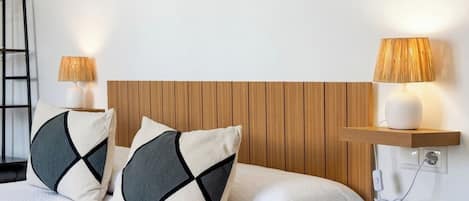 Un lit bien fait, avec deux oreillers, une tête de lit en bois, des lampes de chevet et une prise électrique sur le mur.