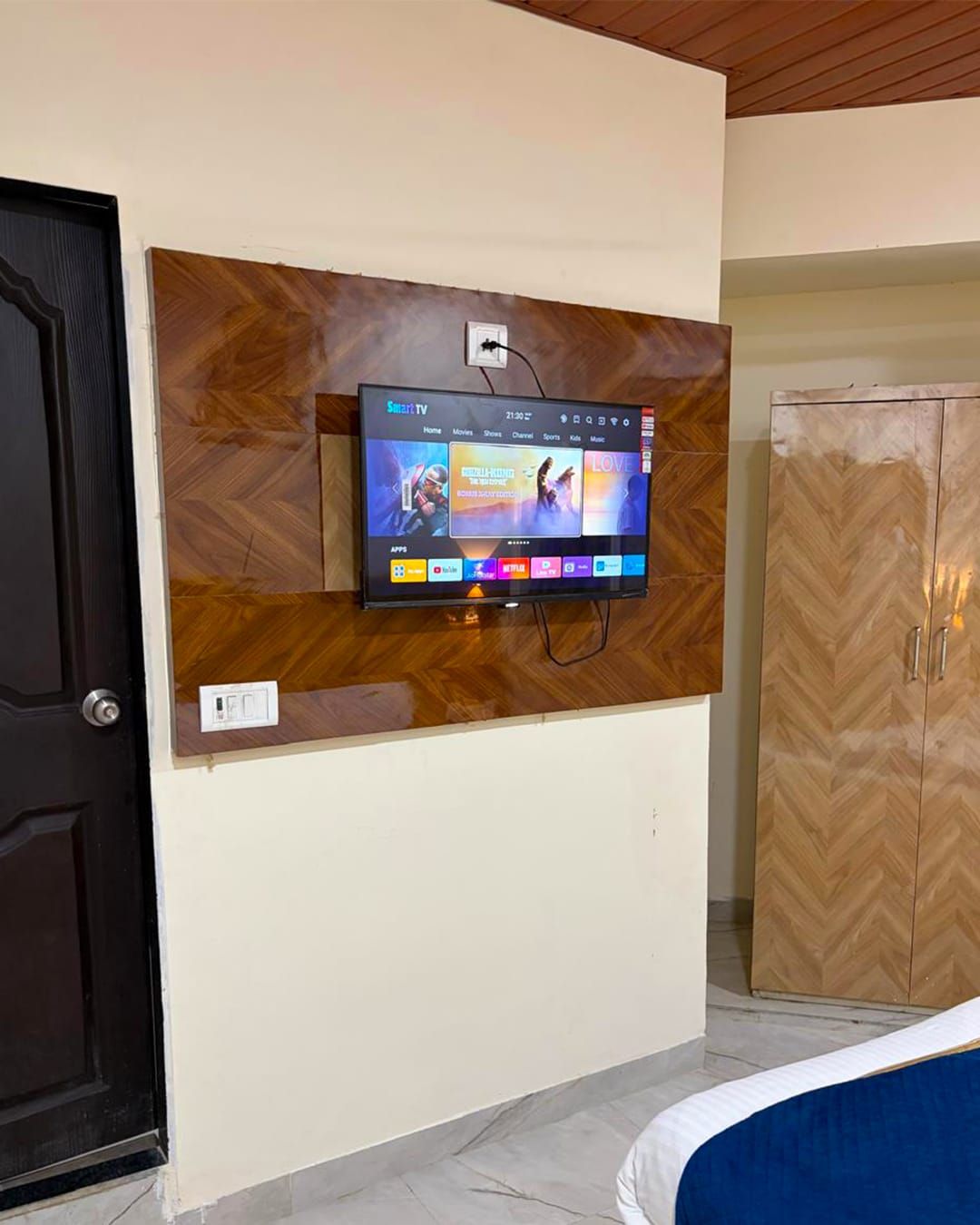 A television mounted on a wall with a wooden panel design, a door to the left, and a wardrobe to the right.