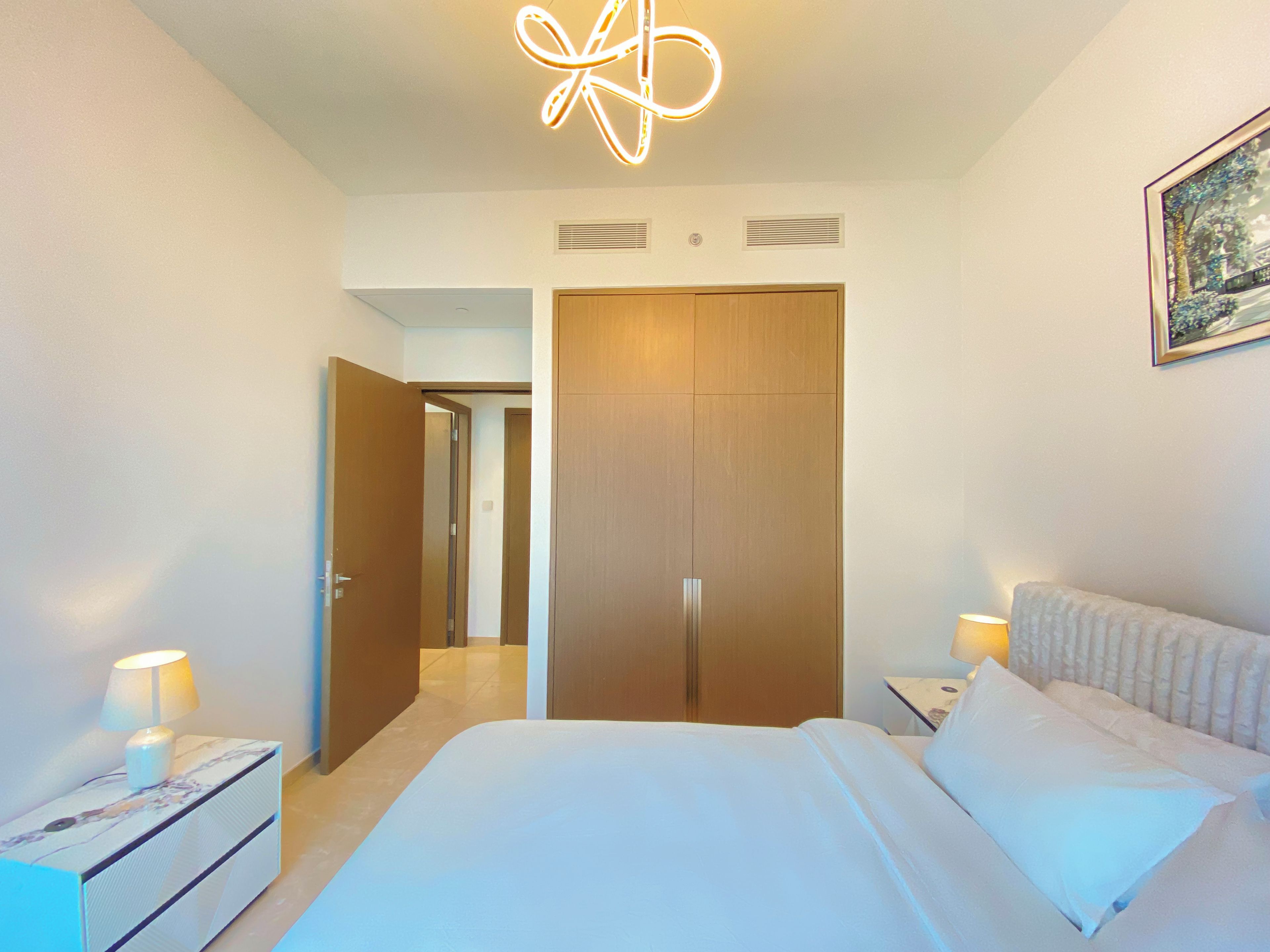 A hotel room with a bed, bedside lamps, a nightstand, a wooden wardrobe, and a ceiling light fixture.