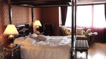 Ein Bett mit Baldachin, zwei Nachttischlampen, eine Chaise Longue und ein kleiner Tisch.