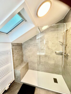 Eine moderne Dusche mit Glasabtrennung, einem Oberlicht darüber und einem weißen Heizkörper.
