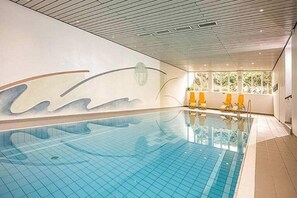 Ein Innenpool mit gefliestem Boden, einem Wellendesign an der Wand und gelben Stühlen am Rand.