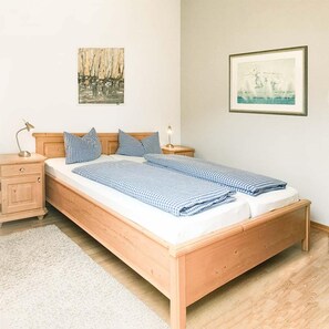 Ein hölzernes Bett mit kariertem Überwurf, ein Nachttisch mit Lampe und zwei an der Wand befestigte Bilder.