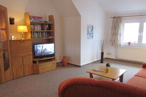 A living room with a television, a bookshelf, a coffee table, and a sofa. - Holiday apartment with 1 bedroom (Wernigerode)