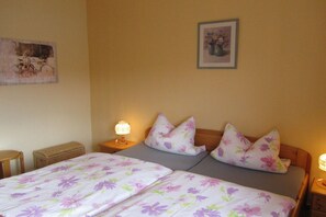 A double bed with floral bedding, two bedside lamps, a wicker basket, and a framed picture on the wall. - Holiday apartment with 1 bedroom (Wernigerode)