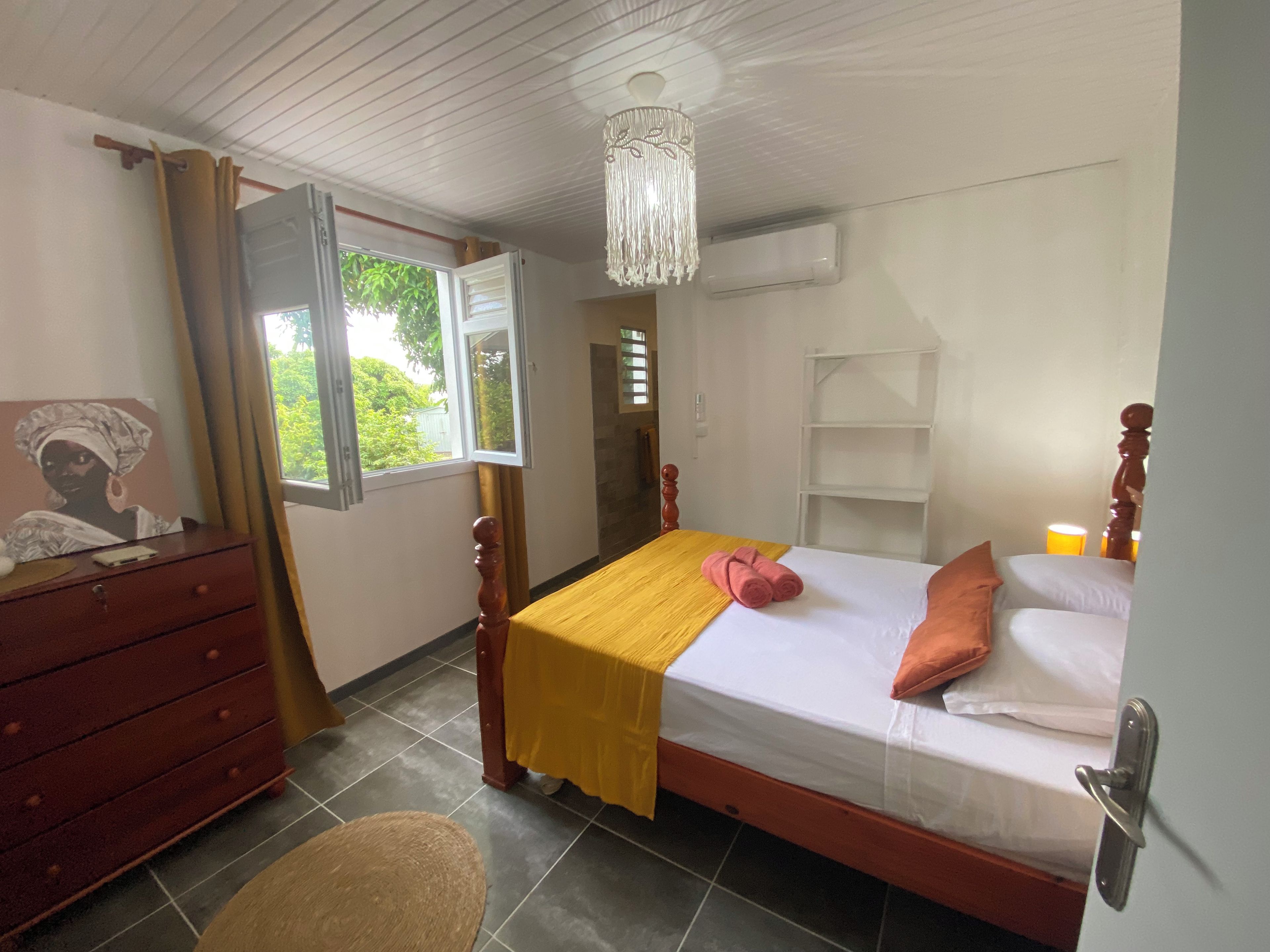 Ein Schlafzimmer mit Bett, Schminktisch, Stuhl, Fenster mit Vorhängen, einer Kristallleuchter und einem Regal.