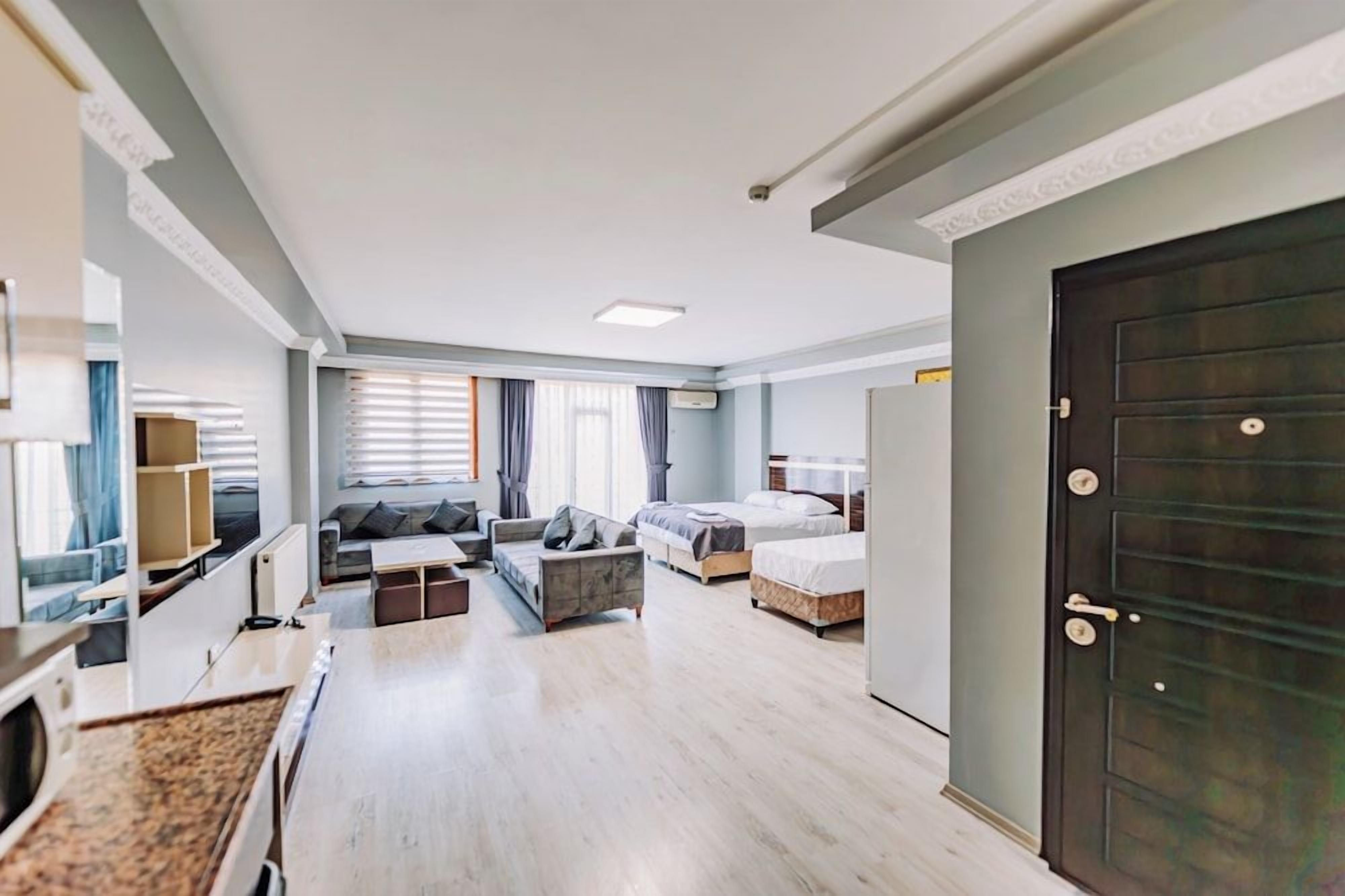 A modern hotel room with a kitchenette, a sofa, a bed, and a large dark door.