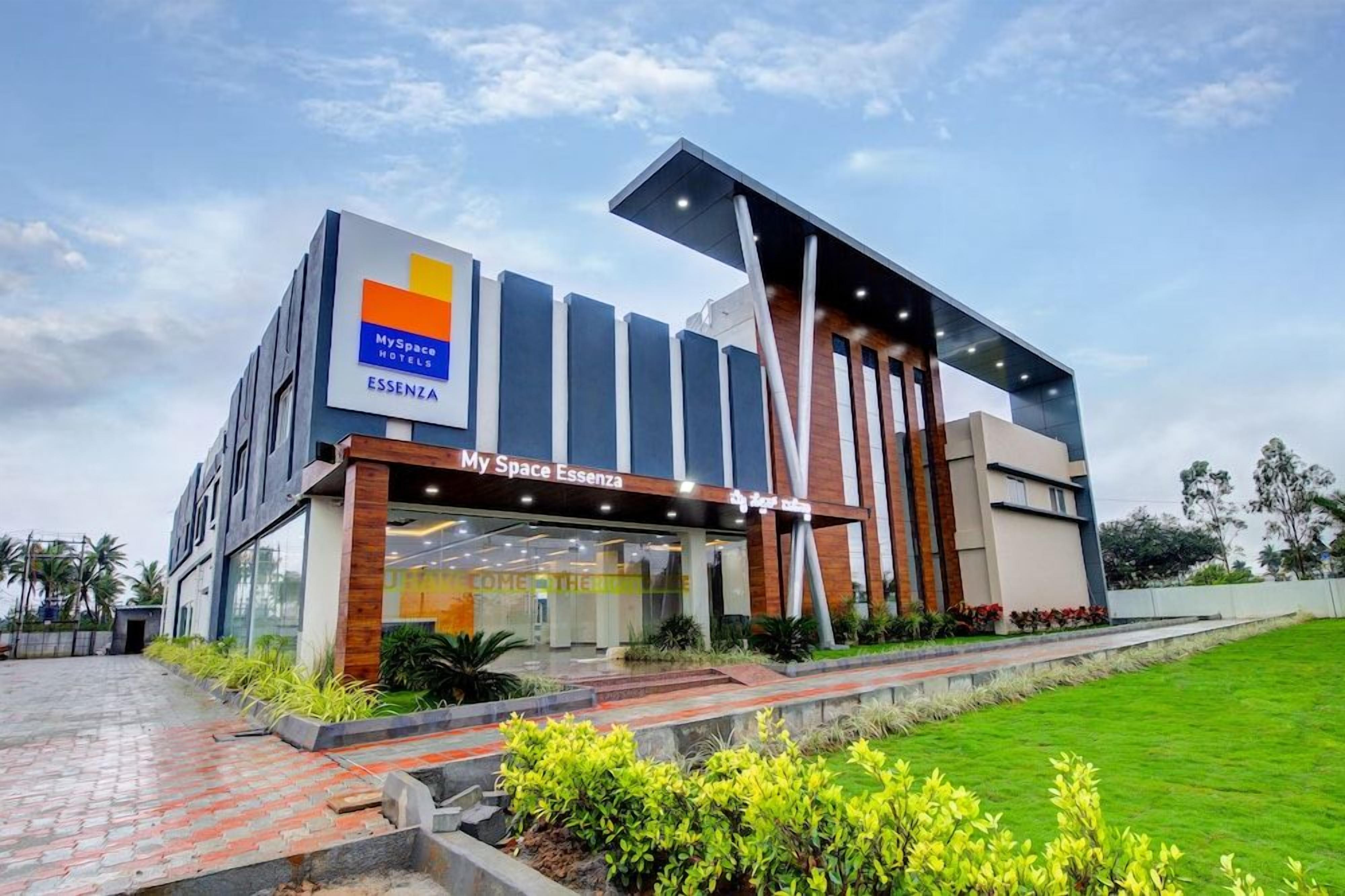 A modern hotel with a MySpace Hotels sign, a large glass entrance, and a well-maintained garden.