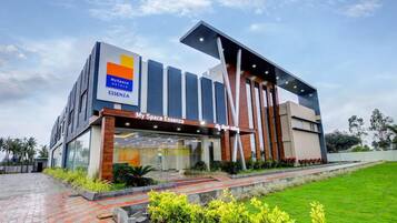 A modern hotel with a MySpace Hotels sign, a large glass entrance, and a well-maintained garden.