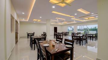 A spacious dining area with multiple tables and chairs, ceiling fans, recessed lighting, and large windows.