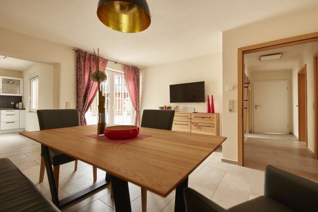 A dining area with a wooden table, chairs, a vase, and a pendant light.
